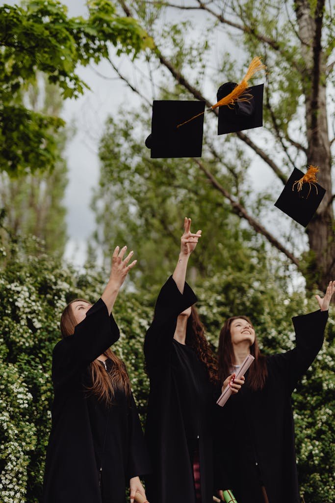 Group of women celebrating graduation by tossing their hats outdoors.